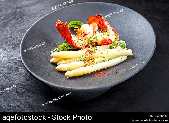 Traditional barbecue spiny lobster tail sliced and offered with white asparagus and lettuce as closeup on a modern design plate