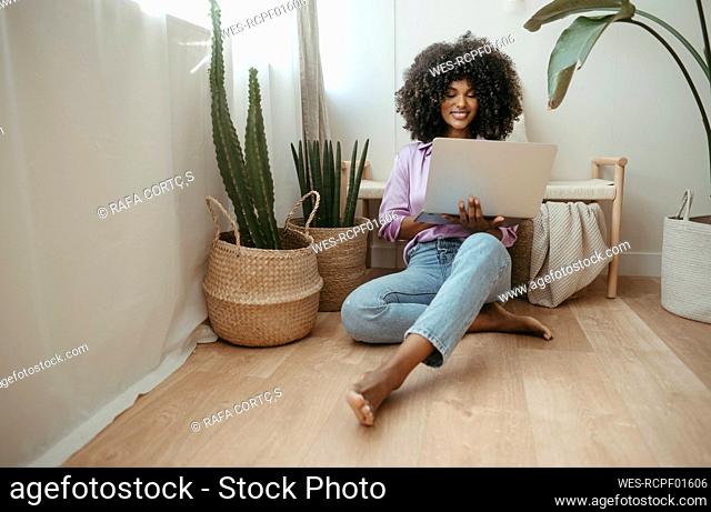 Young woman using laptop sitting on floor in living room