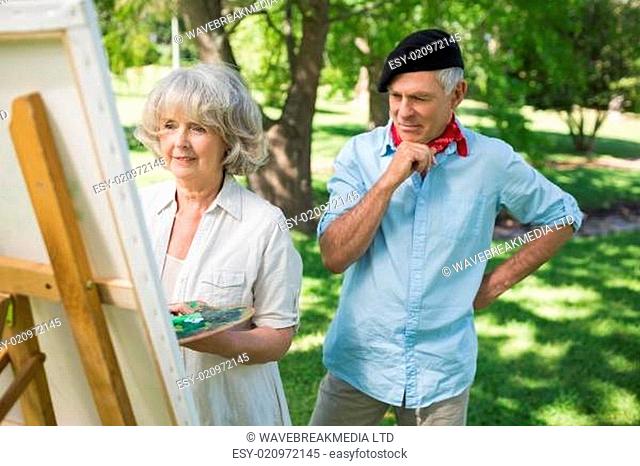 Man watching mature woman paint in park