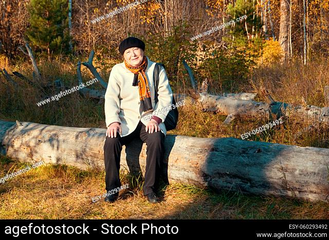 Portrait of kind elderly woman sitting in autumn park, close-up