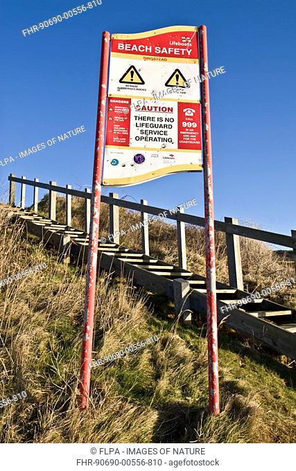 'Beach Safety' and 'Caution, There Is No Lifeguard Service Operating' warning sign beside wooden steps leading to beach, Ringstead Bay, Dorset, England, January