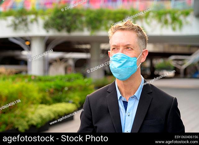 Portrait of mature businessman with mask for protection from corona virus outbreak in the city streets outdoors