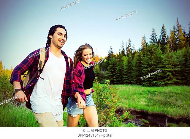 Young couple running while holding hands in a city park in autumn; Edmonton, Alberta, Canada