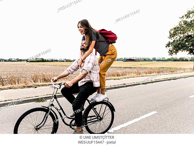 Happy young couple riding together on one bicycle on country road