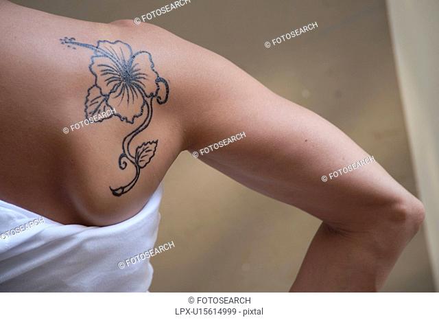 hibiscus flower tattoo on the shoulder of a young woman in a white undershirt