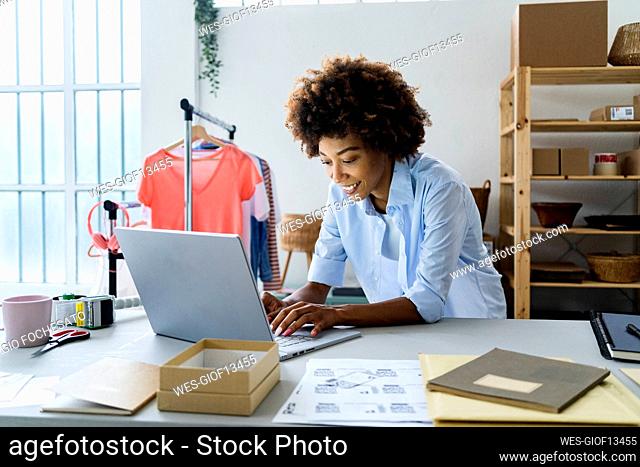Young female fashion designer using laptop while leaning on desk at studio