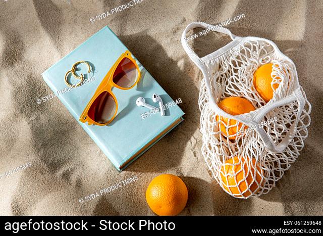 bag of oranges, earbuds and sunglasses on beach