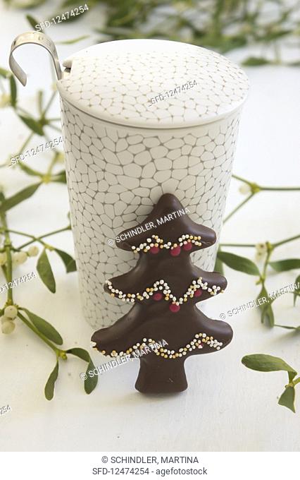 A chocolate-glazed gingerbread Christmas tree with sprinkles against a mug of tea