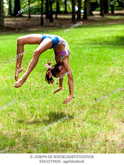 A 10 year old girl doing a back flip in a park