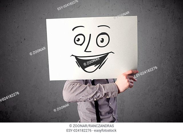Businessman holding a cardboard with smiley face on it in front of his head