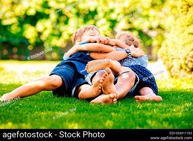 Three little children sitting on a green lawn and talking. Playful siblings at the backyard