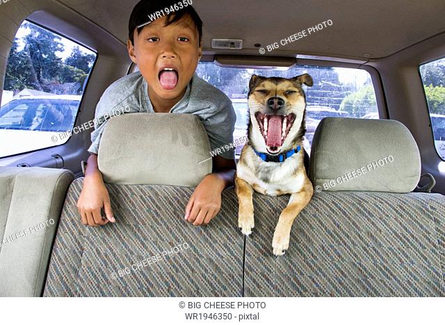 Child and his dog with their mouths open in the backseat of a car