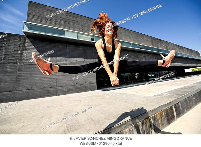 Happy sporty young woman jumping at a modern building