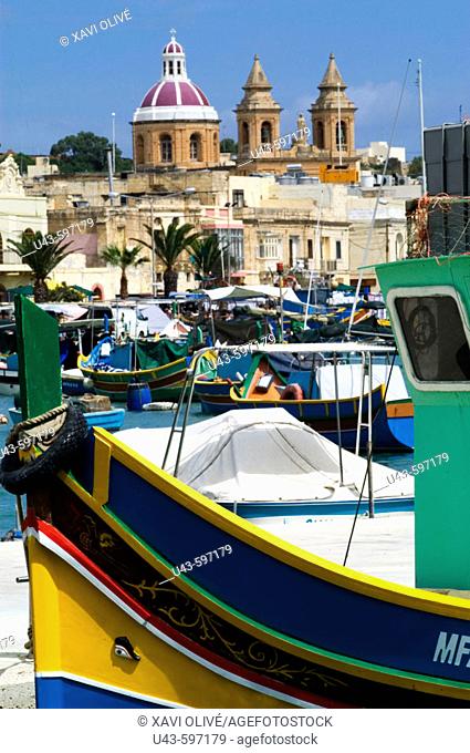 En la imagen, podemos ver en primer término un barco de pesca tradicional maltés, llamado luzzu, con su ojo de Osiris en la proa del barco para auyentar los...