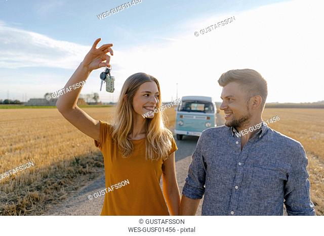 Young couple with car key on dirt track at camper van in rural landscape