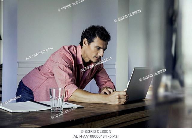Man leaning against table, using laptop computer