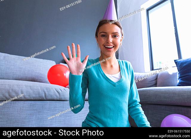 Portrait of woman in party hat smiling and waving at home