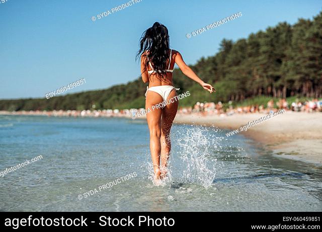young woman in bikini swimsuit running on beach