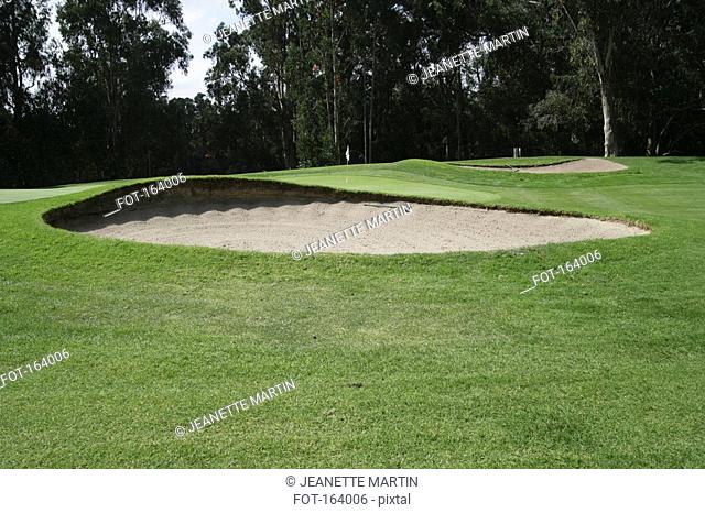 A sand trap in front of a green on a golf course