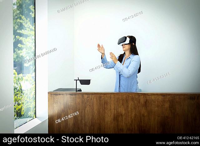 Businesswoman using VR headset behind desk in office