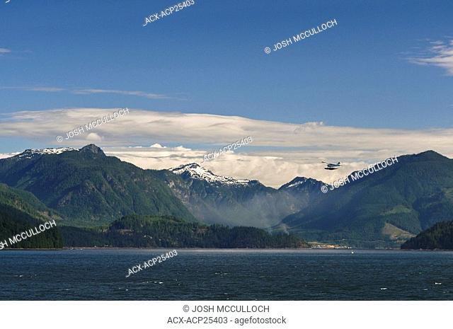 A seaplane flies over Howe Sound with BC's Coast Mountains in the background