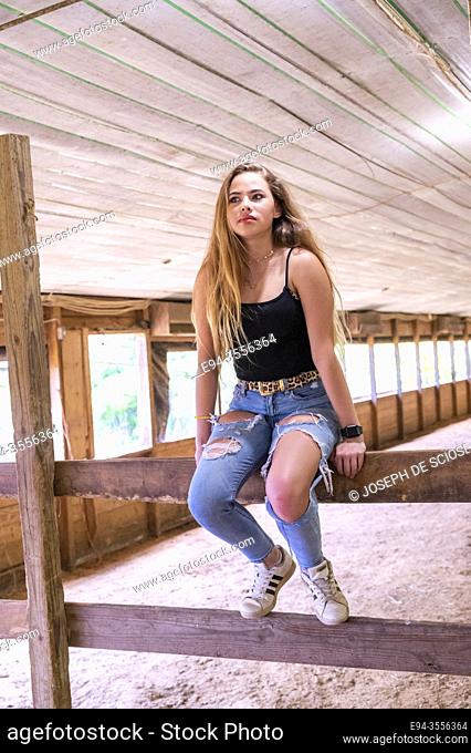 A 14 year old brunette girl in a horse barn looking away from the camera
