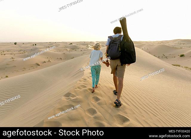 Father holding hand of daughter and walking on sand dune in desert