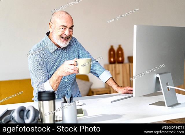 Smiling freelancer holding coffee mug sitting at desk