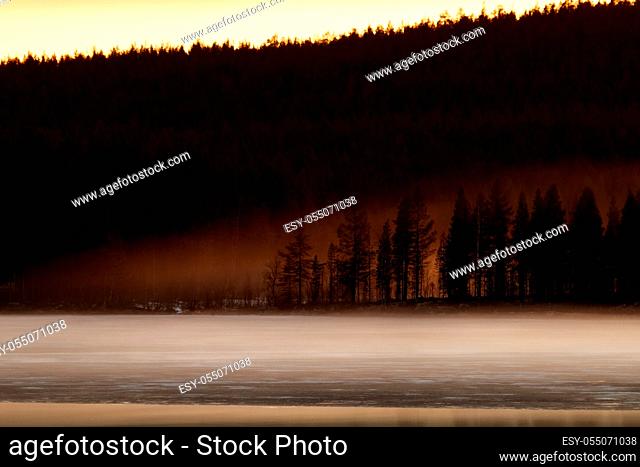 Spring late evening on a lake with fog, remains of ice and disturbing clouds. Foggy lake surrounded by forests
