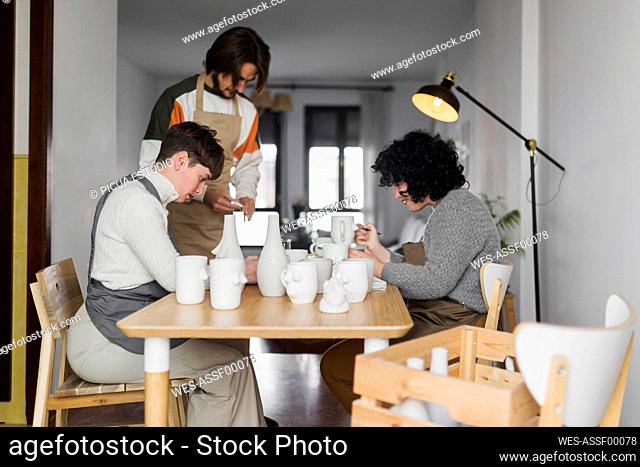 Male and female experts painting ceramics crockery at workplace