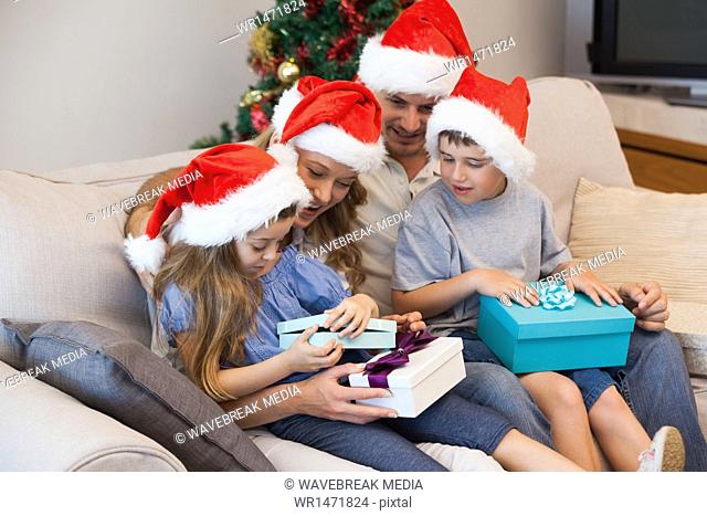 Family in santa hats sitting on sofa with gift boxes in living room