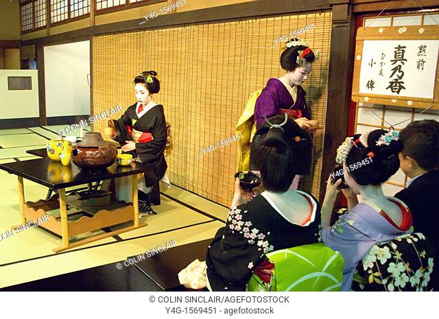 Two geisha one in full Spring kimono and hair ornaments preparing and serving tea to tea ceremony guests  Location is the Gion geisha quarter of Kyoto
