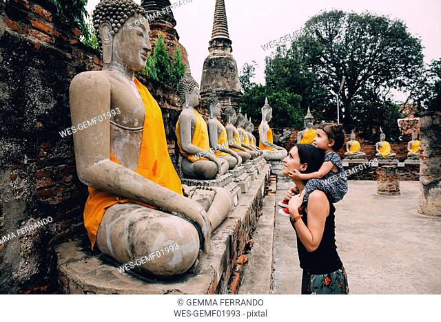 Thailand, Bangkok, Ayutthaya, Buddha statues in a row in Wat Yai Chai Mongkhon, mother and daughter in front of a buddha statue