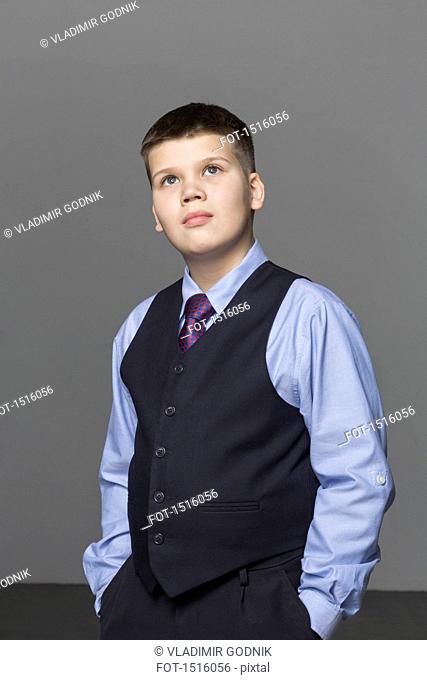 Confident boy looking up while standing against gray background