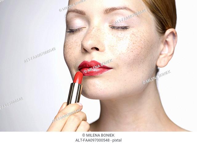 Young woman putting on lipstick