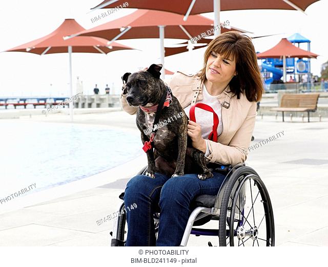 Woman sitting in wheelchair at waterfront with dog in lap