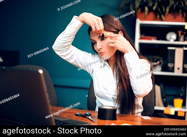 Bored lady trying to stay awake in her office. Crazy female office worker stick taping her eyelids so that she wont fall asleep while working at computer