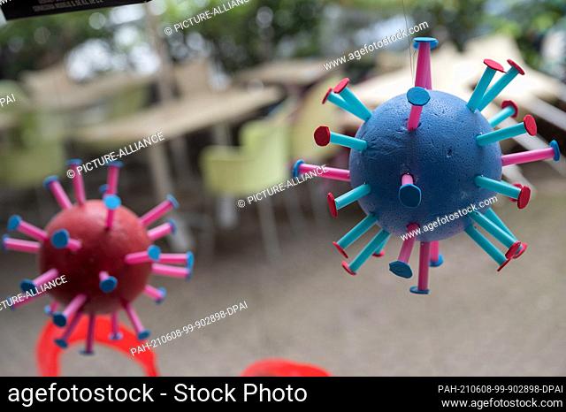 dpatop - 07 June 2021, Hessen, Frankfurt/Main: Stylized Corona viruses hang in a shop window, while in the background chairs and tables are placed in front of a...