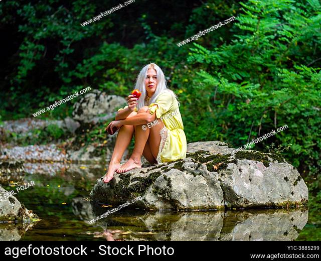 Attractive blonde woman on a Green forest river with an apple in hand