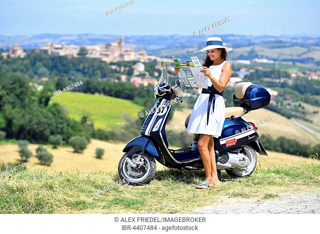 Fashionable woman looking at map with Vespa Primavera scooter, Corinaldo, Marche, Italy
