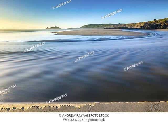 The river on Gwithian Beach in Cornwall, captured shortly before sunset with Godrevy Lighthouse in the distance