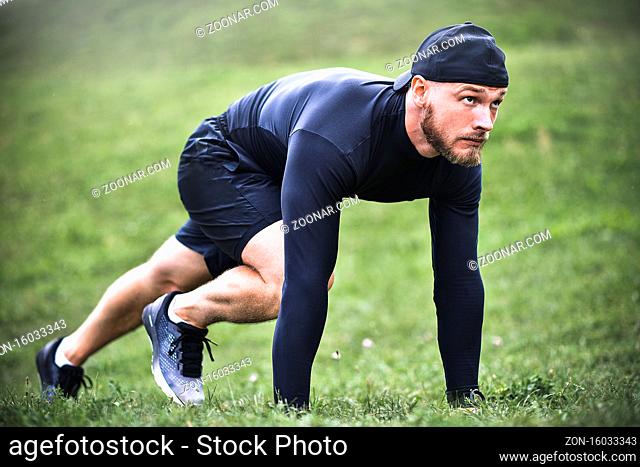 Muscular sportsman stretching out before a sports training at the street in city park