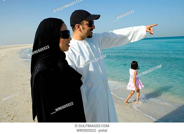 Young couple with daughter on beach, pointing, smiling