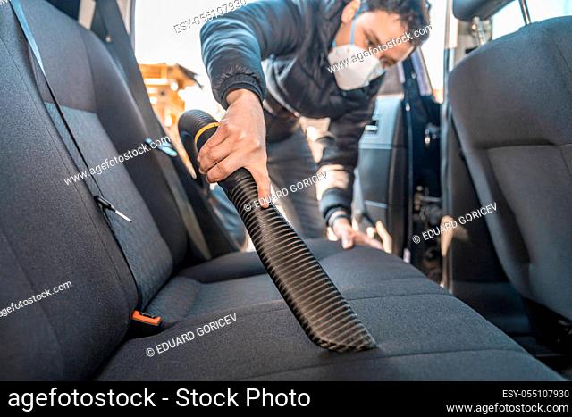 vacuuming the interior of a car with a respirator on the face during a coronavirus epidemic