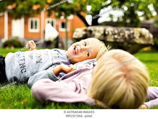 Happy boy lying on his sister's stomach in yard