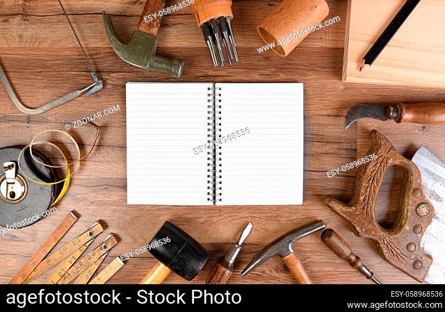 High angle closeup of a large group of tools arranged around an open note book with blank pages