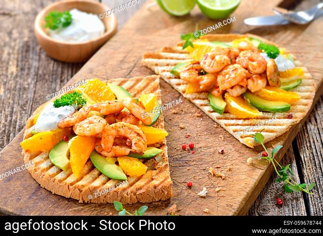 Großer Toast mit Shrimps vom Grill auf Avocado und Orangenstücken angerichtet, dazu Sauerrahmsauce mit Limettensaft und Dill- Toast with grilled prawns on...
