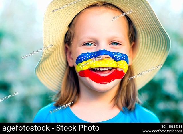 Laughing little girl in straw hat with painted face having fun. Outdoor portrait