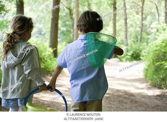 Children walking in woods together with butterfly net and bucket