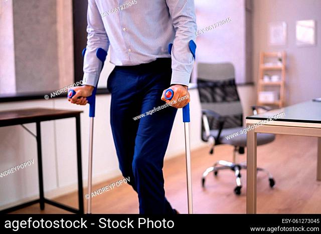 Worker With Crutches At Workplace Or Office. Handicap Rehabilitation Benefits